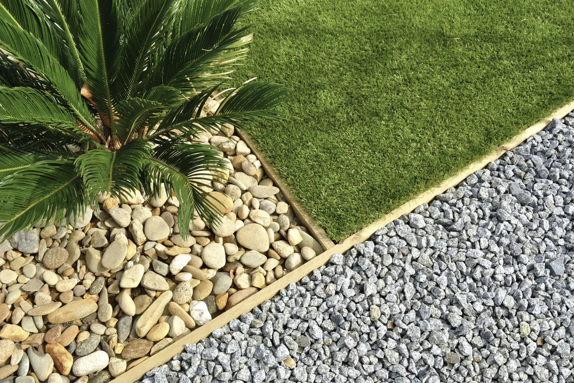 A garden corner with grass, stones, and gravel separated by a stone border.